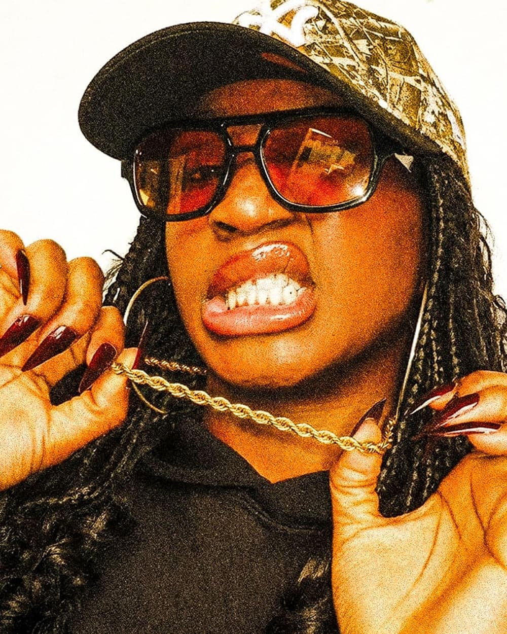 Person wearing sunglasses and a cap, holding a gold chain